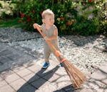 A cute child sweeping a garden pathway with a broom under sunny weather.